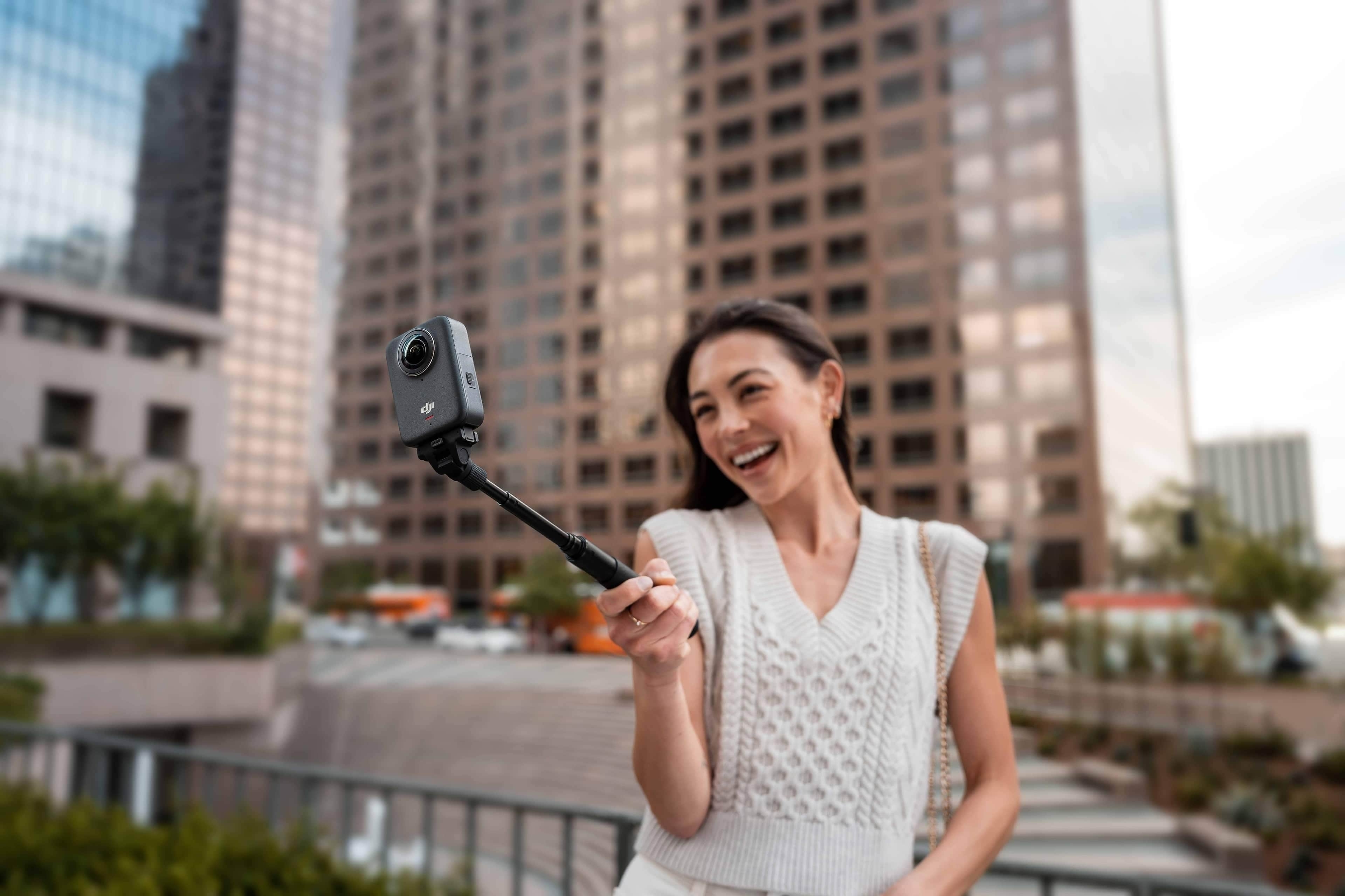 Frau hält den DJI Osmo 70cm Invisible Selfie Stick in einer urbanen Umgebung und lächelt.
