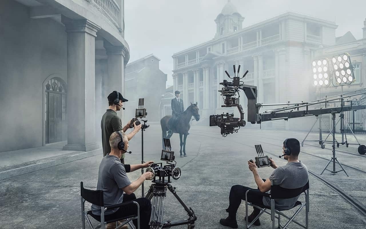 Professionelles Set mit DJI Transmission, Kameraleuten und einem Darsteller auf einem Pferd bei einer Filmaufnahme.