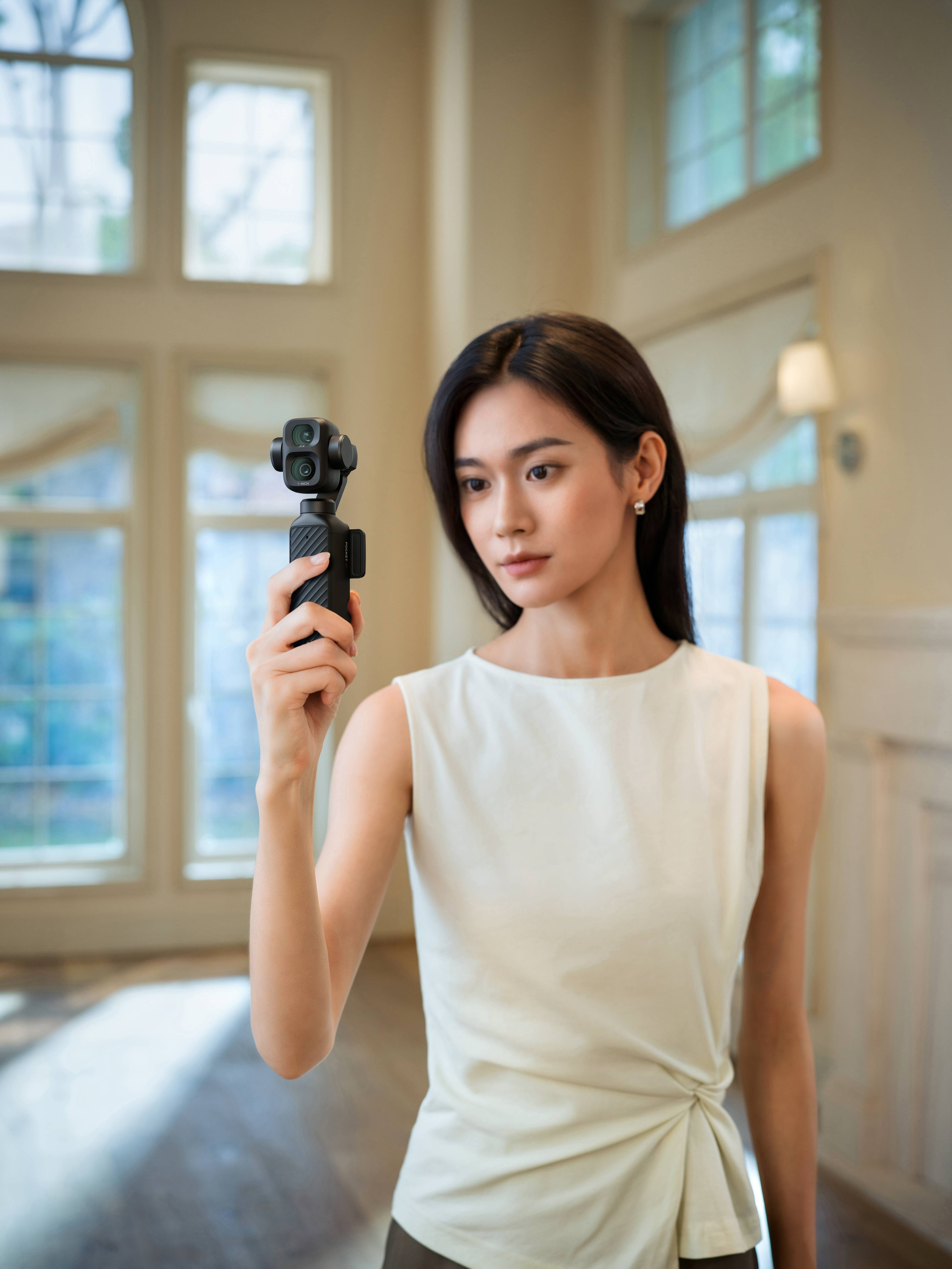 Frau hält die DJI Osmo Pocket 4P Standard Combo für Videografie in hellem Raum mit großen Fenstern.