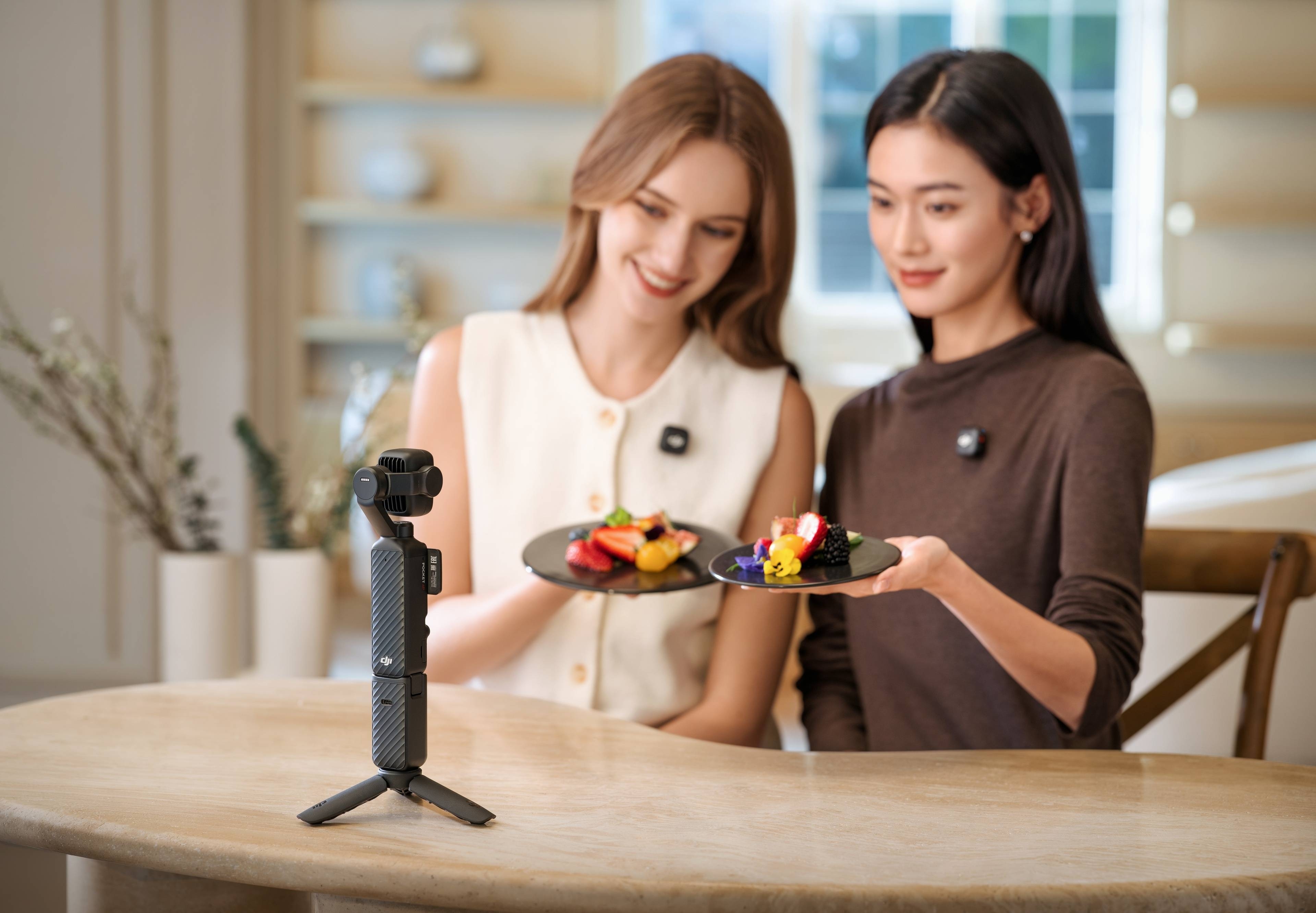 Zwei Frauen präsentieren bunte Teller mit Snacks neben der DJI Osmo Pocket 4P Standard Combo auf einem Tisch.