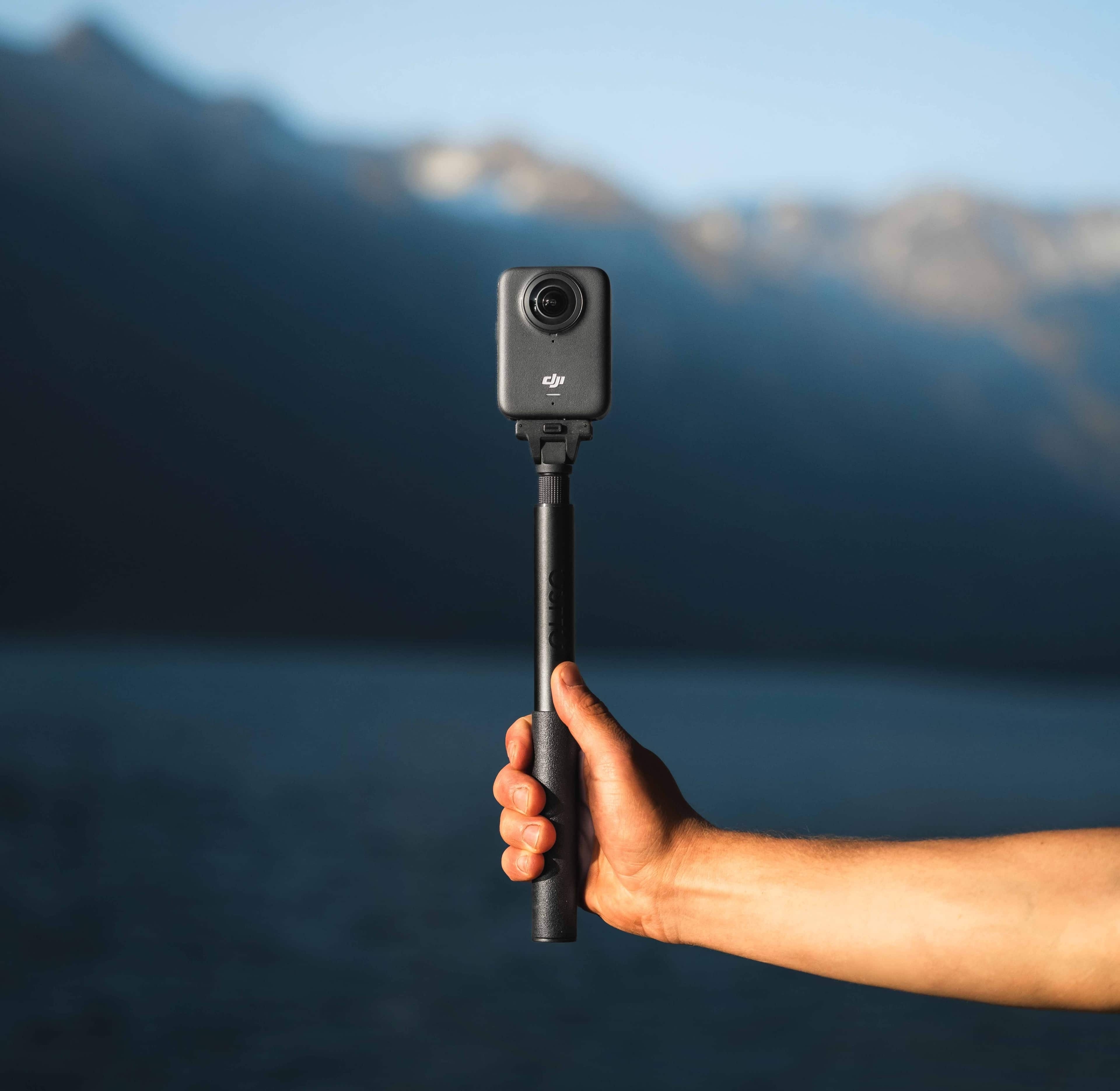 DJI Osmo 1.2m Invisible Selfie Stick Kit in der Hand mit Landschaft im Hintergrund.