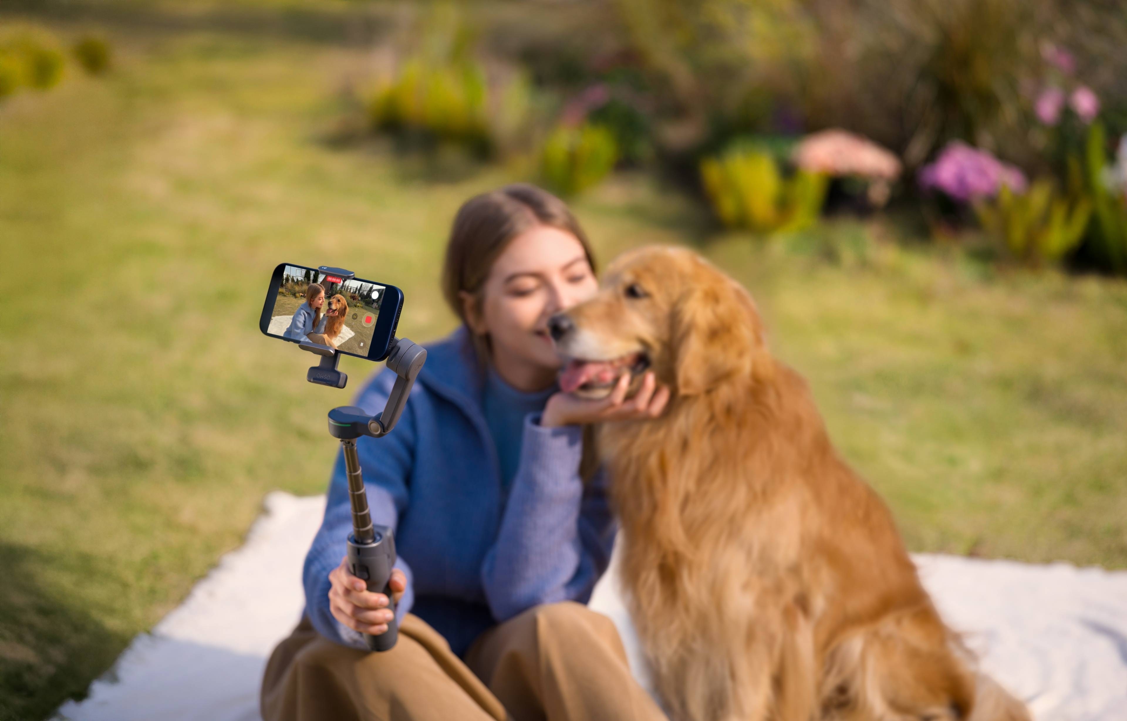 Frau mit DJI Osmo Mobile 8P Standard Combo und Hund im Freien, lächelnd auf einer Decke sitzend.