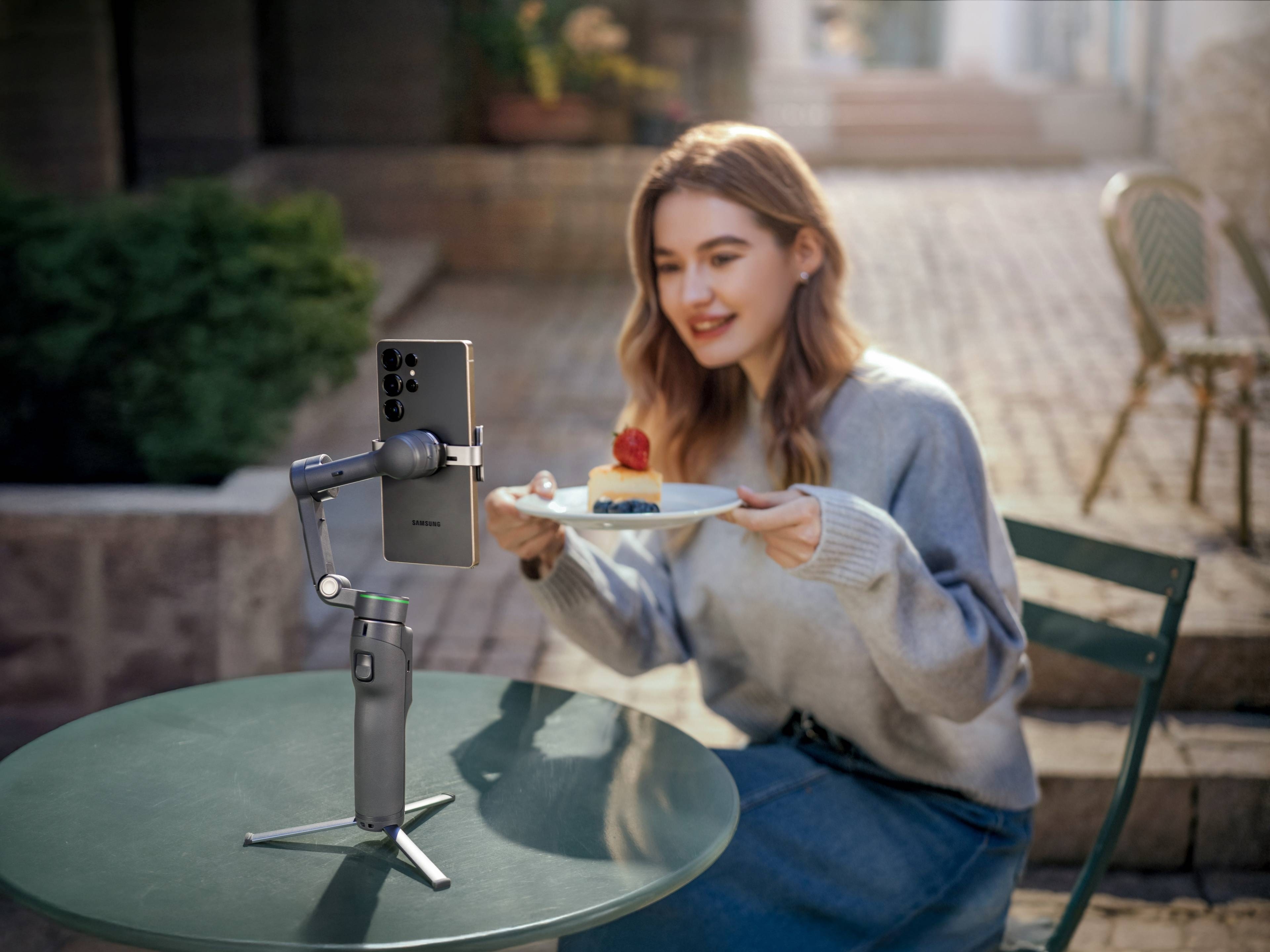 DJI Osmo Mobile 8P Creator Combo: Gimbal mit Smartphone, einer Frau mit Dessert am Tisch im Freien.