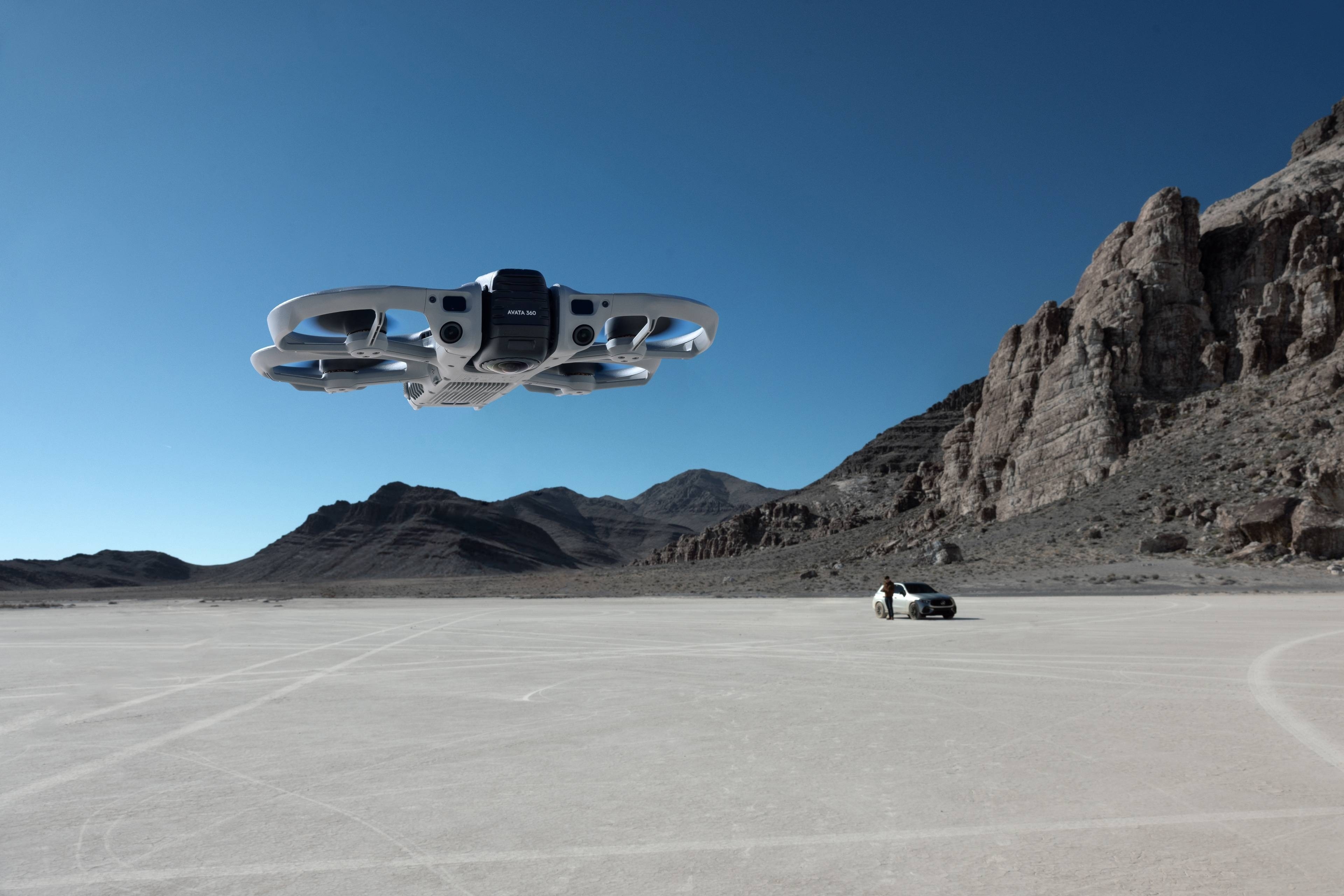 DJI Avata 360 Fly More Combo (DJI RC 2) schwebt über einer kargen Landschaft mit einem Fahrzeug im Hintergrund.