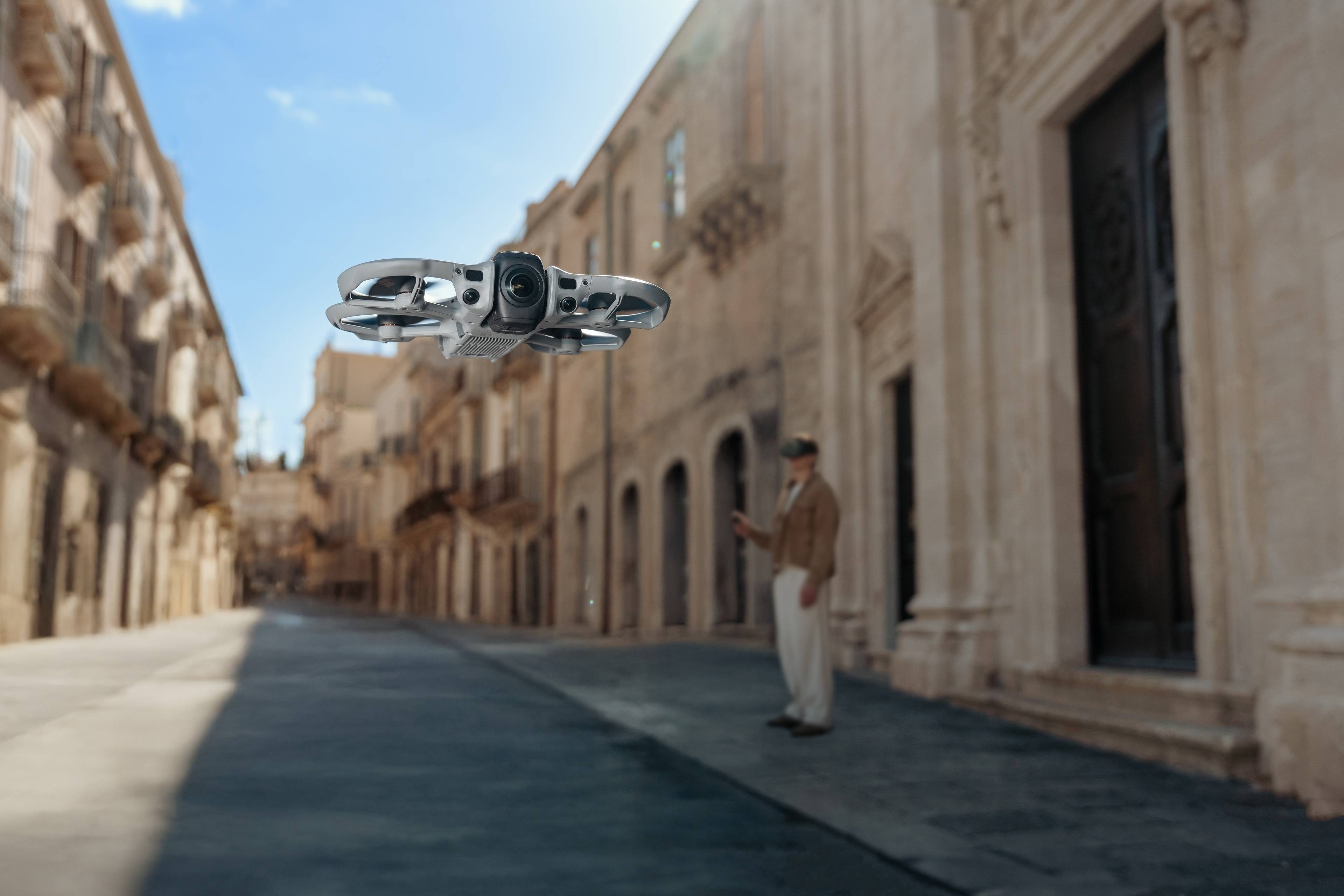 DJI Avata 360 Fly More Combo (DJI RC 2) fliegender Mini-Drohne in Stadtstraße mit historischem Hintergrund.