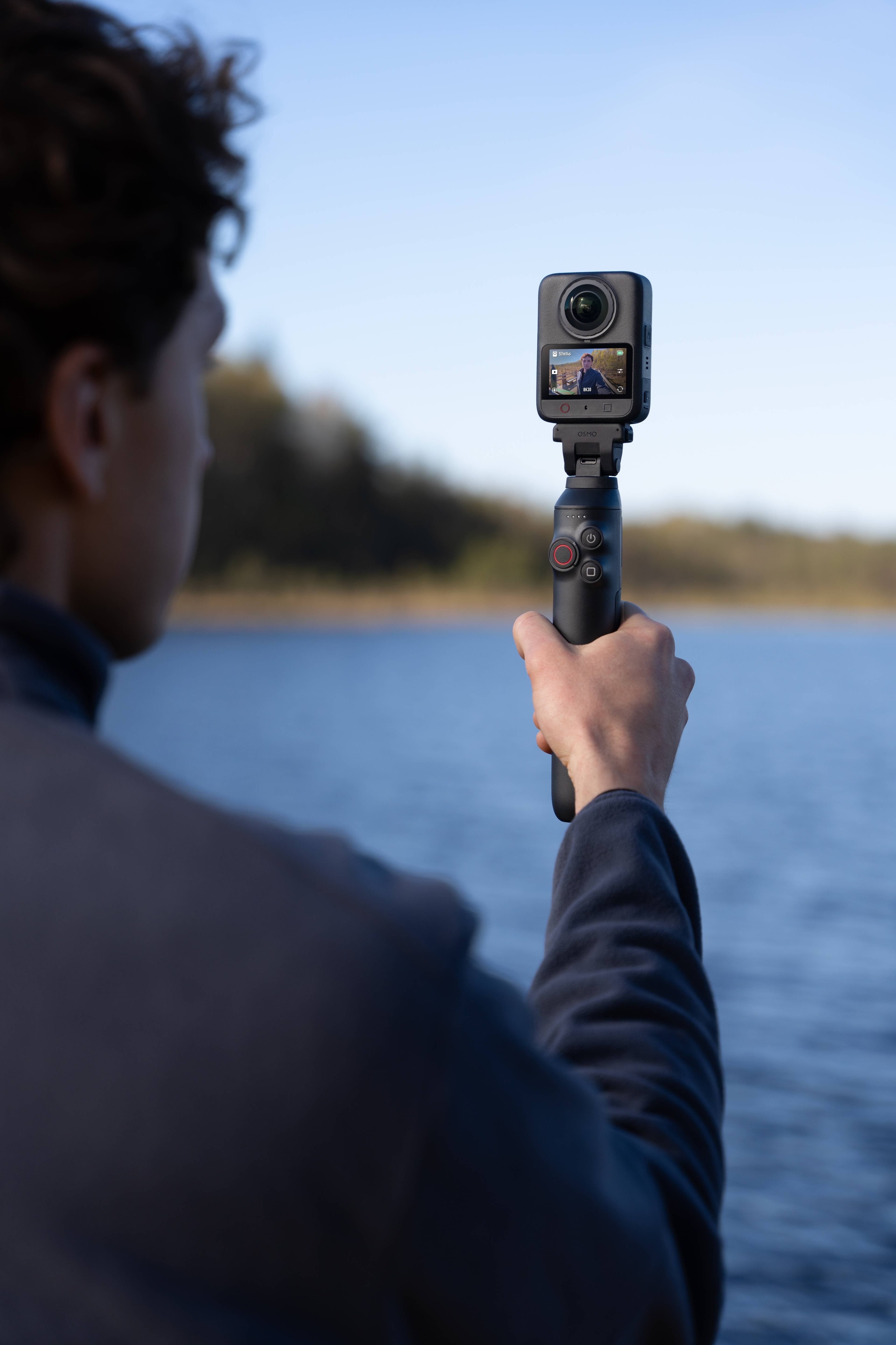 Person hält die DJI Osmo 360 II am See, zeigt die kompakte Kamera in Aktion.